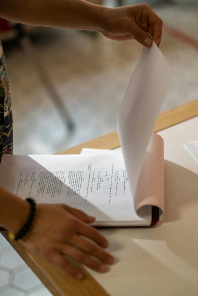 Hands flipping through a printed screenplay on a light-colored table indoors.